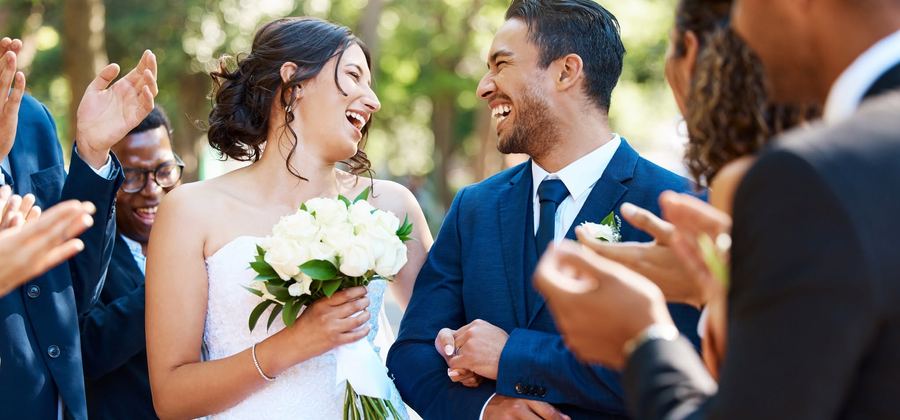 A bride and groom laughing with guests clapping around them on the lawn