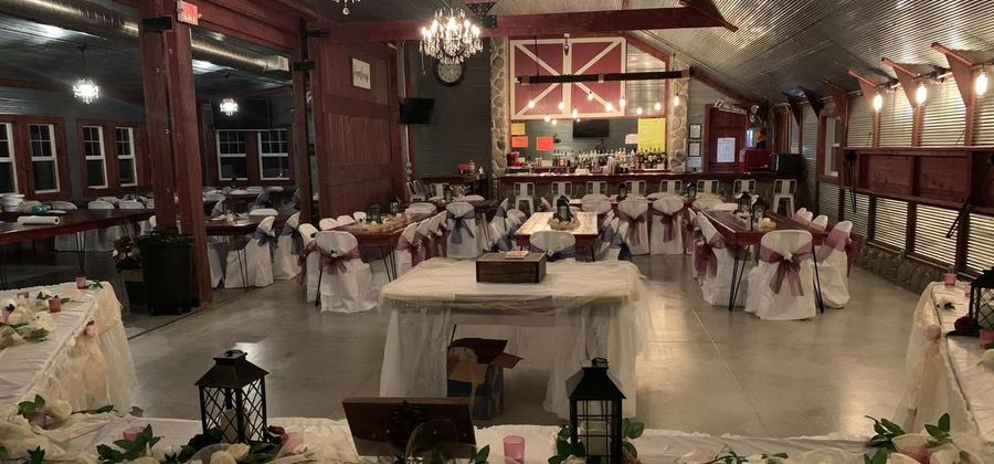 Red barn hall with chandeliers and long tables set for a wedding reception